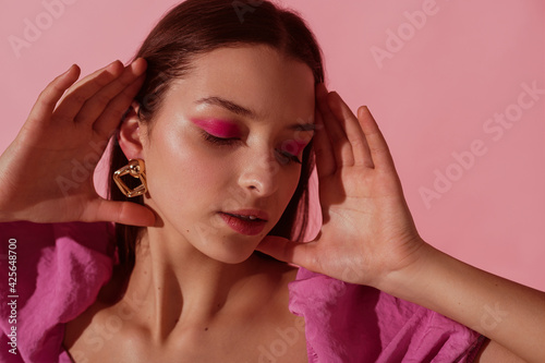 Vászonkép Close up beauty portrait of young beautiful woman with pink, fuchsia color eyeshadow makeup, flawless clean skin, wearing elegant golden earrings, pink blouse