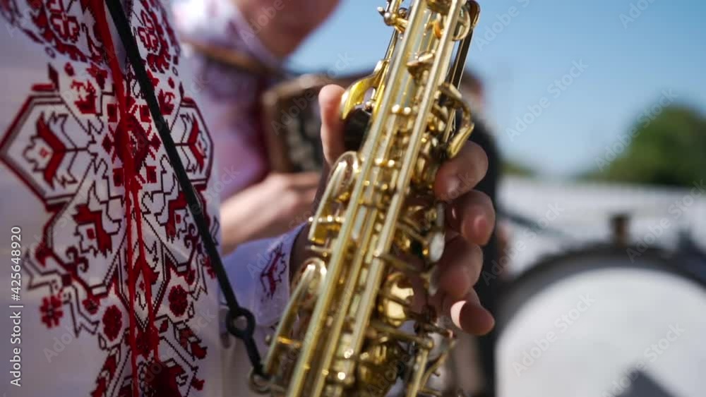 A caucasian man in an embroidered shirt plays a wind musical instrument saxophone pressing his fingers on the keys and the valves open and close and music is heard A caucasian man in an embroidered shirt plays a wind musical instrument saxophone pressing his fingers on the keys and the valves open and close and music is heard