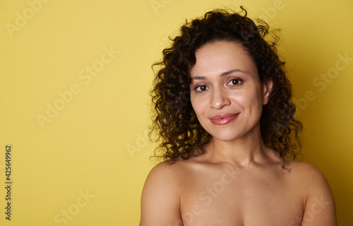 Young hispanic woman with curly hair cute smiling at the camera while standing on yellow background with copy space