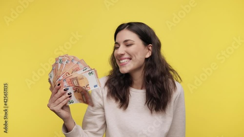 Attractive young female holding cash euro in hands. Caucasian girl hold fan of cash money in euro banknotes. Woman 20s in casual light sweat shirt posing isolated on yellow background studio with cash