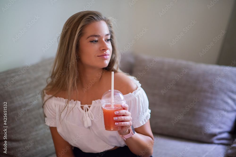 Woman using a straw to drink grapefruit juice while watching television Woman using a straw to drink grapefruit juice while watching television