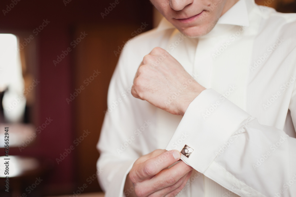 Groom's morning. Wedding preparing. Man in white shirt putting on cufflinks. Business dress code