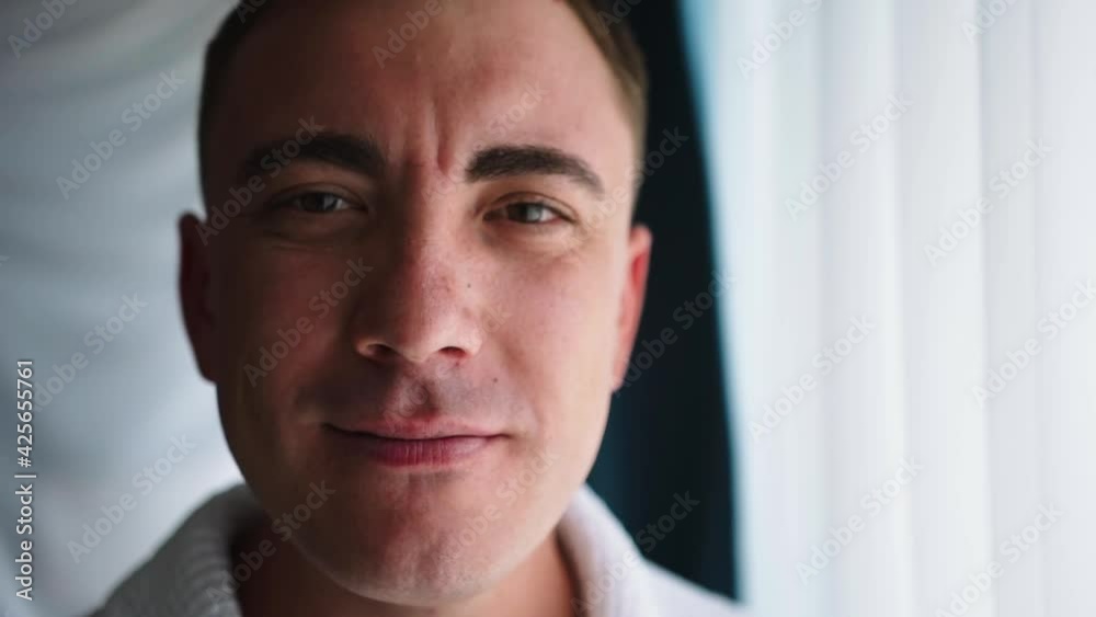 Charismatic attractive adult man with a good appearance stands by the window and looks at the camera. A masculine expression face with a light sexy tender smile with a closed mouth Charismatic attractive adult man with a good appearance stands by the window and looks at the camera. A masculine expression face with a light sexy tender smile with a closed mouth
