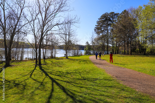 people walking down a hiking trail near a lake with lush green grass and trees along the path with blue lake water and blue sky  at Lake Horton Park in Fayetteville Georgia photo