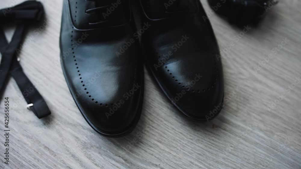 Black classic men's shoes with laces stand on the floor on the laminate and next to a black belt and a bow tie. Details of wardrobe accessories for formal outfit. Close-up Black classic men's shoes with laces stand on the floor on the laminate and next to a black belt and a bow tie. Details of wardrobe accessories for formal outfit. Close-up