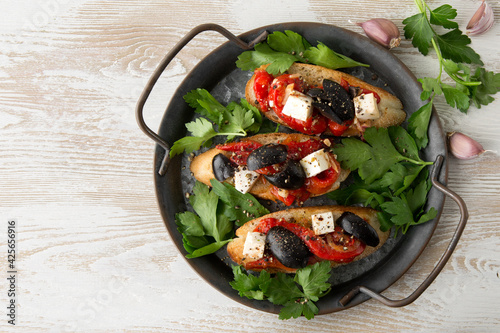 bruschettas with feta cheese, baked pepper, olives and parsley on a tray on a light table