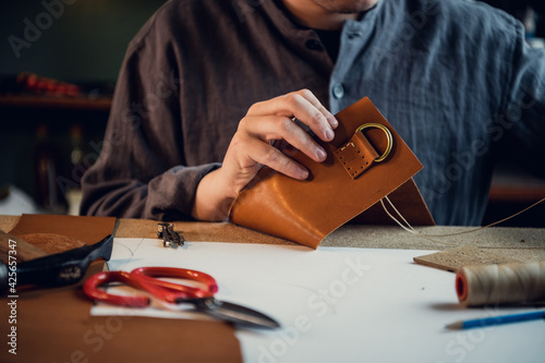 Close-up photo the hands of a skilled shoemaker make a bag from a piece of genuine leather