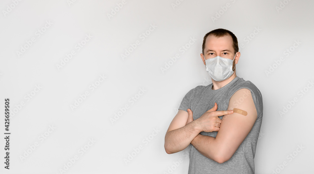 A young adult man wearing a protective face mask shows his arm after vaccination. Theme immunization during pandemic covid-19. Space for text, selective focus A young adult man wearing a protective face mask shows his arm after vaccination. Theme immunization during pandemic covid-19. Space for text, selective focus