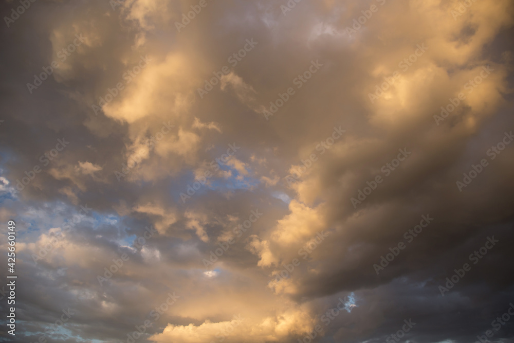 Epic sunset storm sky. Big white grey cumulus thunderstorm clouds in yellow orange sunlight on blue sky background texture