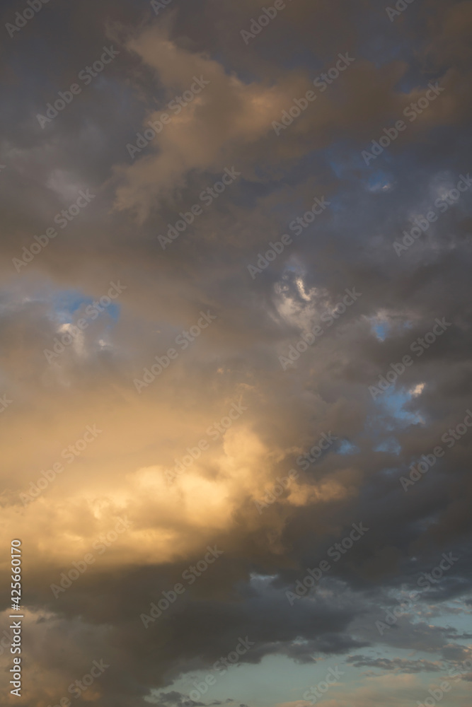 Epic sunset storm sky. Big white grey cumulus thunderstorm clouds in yellow orange sunlight on blue sky background texture	
