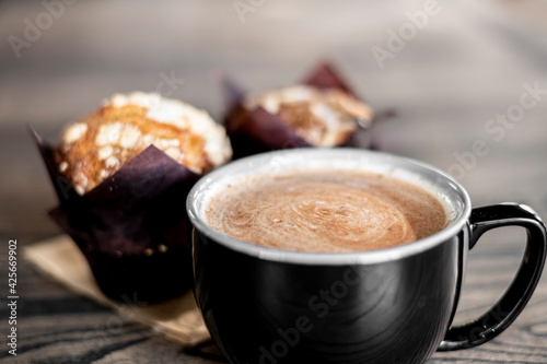Hot coffee cappuccino latte spiral foam with blueberry muffins in the background blurred