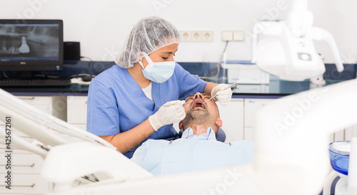 Female dentist in face mask with male patient during checkup at dental clinic office