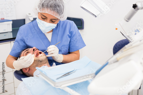 Professional dentist woman inspects patient teeth with dental tools - mirror and probe