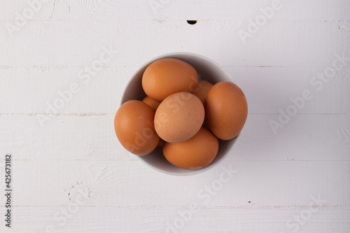 Organic eggs in a white bowl over white wooden table