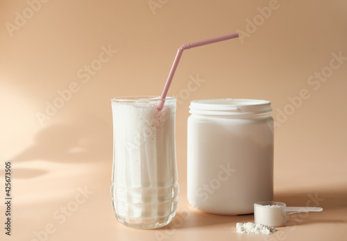 whey drink in a high glass. whey protein vanilla cocktail. a jar with protein powder and a scoop of powder on a table. morning drink for health and beauty