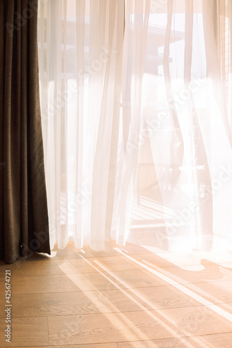 Modern room interior with an open window in minimal style. Transparent tulle with morning sun rays on shadow background. Vertical photo.
