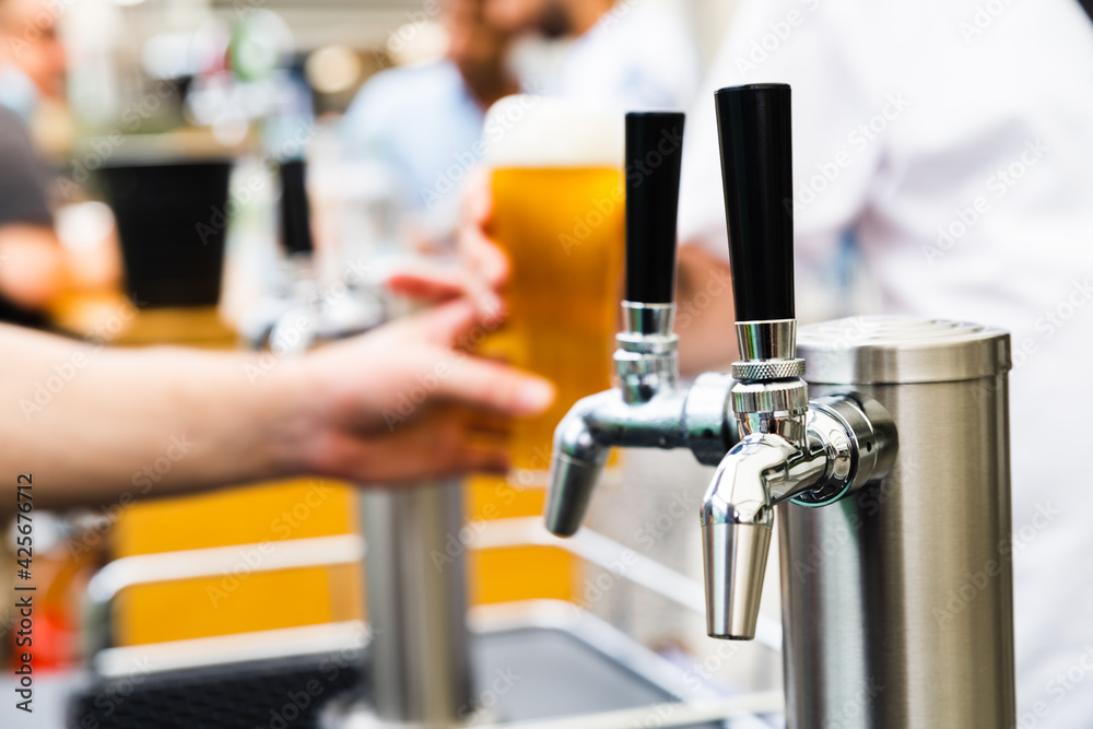 Silver Beer taps with black handles covered in condensation with a hand serving a tall glass of amber coloured beer in the background with a perfect head Silver Beer taps with black handles covered in condensation with a hand serving a tall glass of amber coloured beer in the background with a perfect head