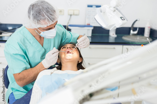 Dentist man examining a latin female patient teeth with dental tools - mirror and probe
