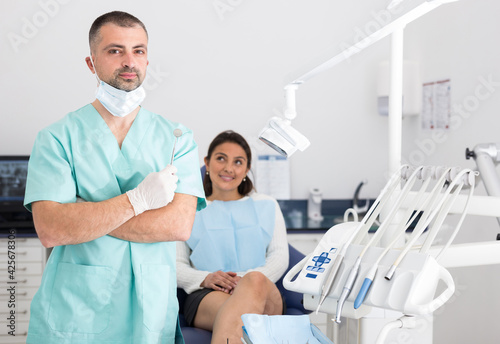 Positive male dentist in face mask standing near patient and preparing for treatment