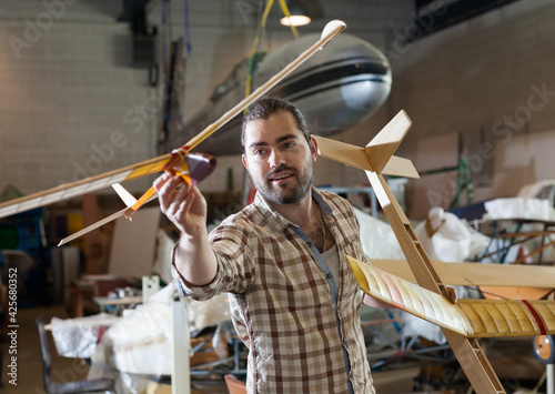 Cheerful male aircraft enthusiast holding sports airplane models in workshop