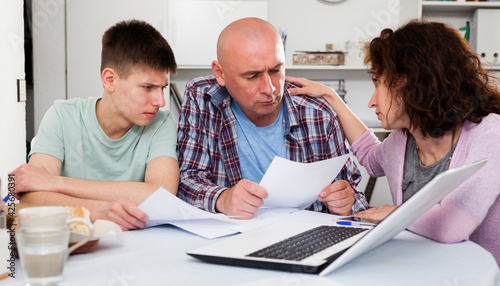 Upset man with his wife and teen son reading documents at home table