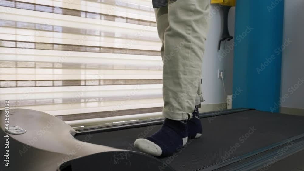 Low angle view of a patient's feet as they slowly walk on a treadmill during a physical rehabilitation session. Low angle view of a patient's feet as they slowly walk on a treadmill during a physical rehabilitation session.