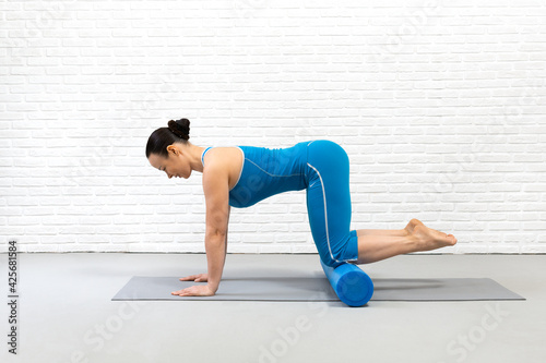 Adult caucasian woman practice pilates with props in fitness studio indoor, bird dog drill with foam roller under her knees, starting position, selective focus.