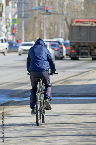 A man rides a bicycle on a city sidewalk on a sunny spring day