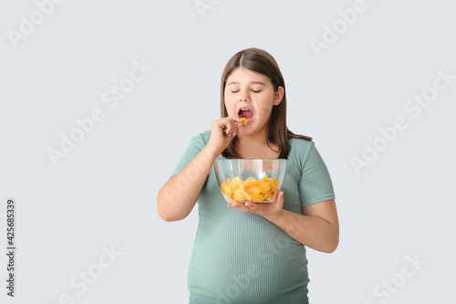 Overweight girl eating tasty chips on light background