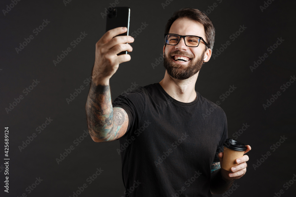 Happy man in earphones taking selfie on cellphone while drinking coffee Happy man in earphones taking selfie on cellphone while drinking coffee
