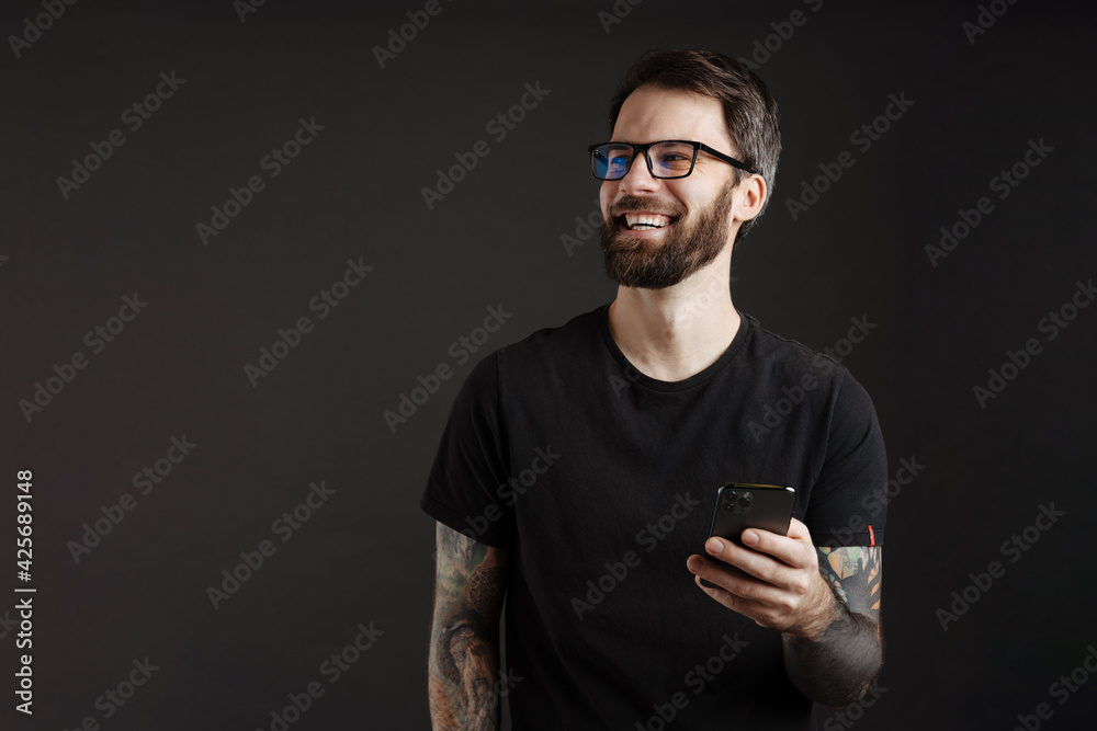 Bearded happy man in eyeglasses smiling and using cellphone