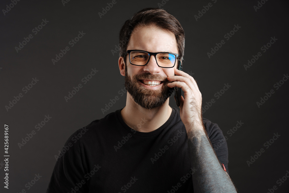 Bearded happy man in eyeglasses smiling and talking on cellphone Bearded happy man in eyeglasses smiling and talking on cellphone