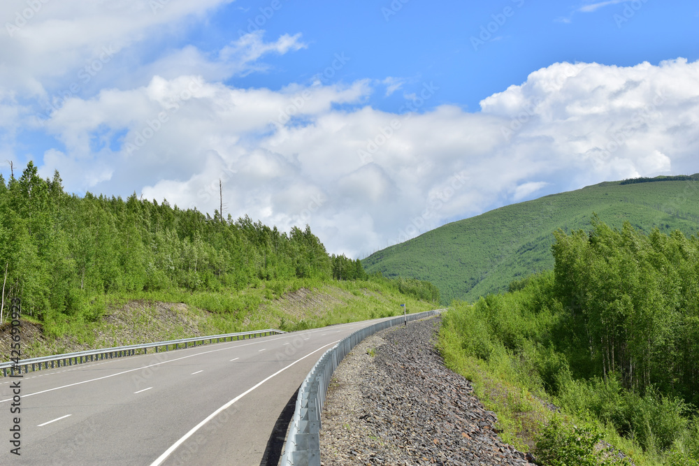 An asphalt road among the green hills. A bright summer day. Sikhote-Alin Mountains.