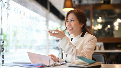 Confident businesswoman talking by speakerphone while sitting in modern office.