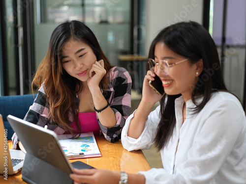 University student talking on the phone while doing assignment with her friend in cafe