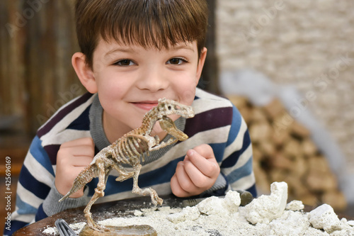 Happy child digging the dinosaur and having fun with archaeology excavation kit. Boy plays an archaeologist excavated, training for dig fossil