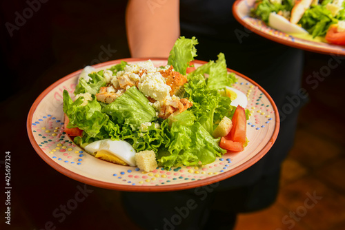 Caesar Salad in ceramic plate served by waiter in restaurant or diner.