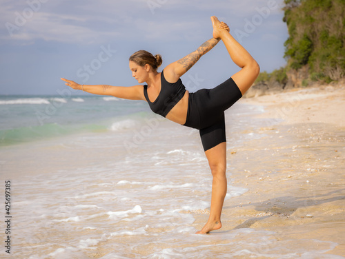 Outdoor yoga. Attractive woman practicing yoga, standing in Natarajasana, Lord of the Dance Pose. Balancing, back bending asana. Exercise on the beach. Thomas beach, Bali