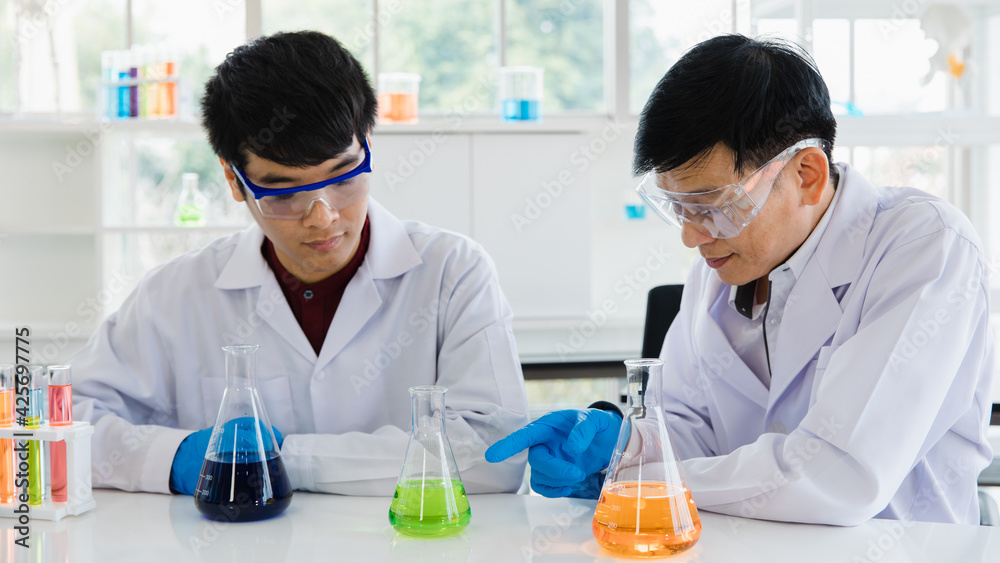Portrait 2 adults scientist asian men sitting and smiling feel happy and confident looking at camera in laboratory room at the morning. More glassware, test tube with liquid chemical put on table Portrait 2 adults scientist asian men sitting and smiling feel happy and confident looking at camera in laboratory room at the morning. More glassware, test tube with liquid chemical put on table