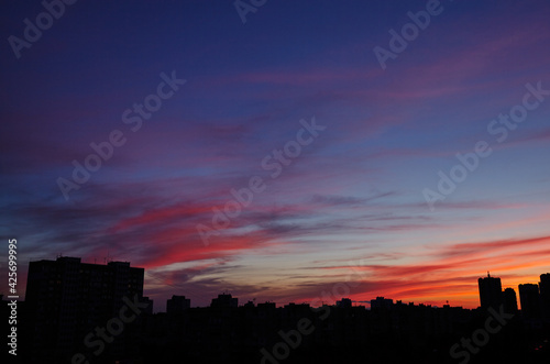 Colorful dramatic sky with clouds at sunset. City during warm sunset