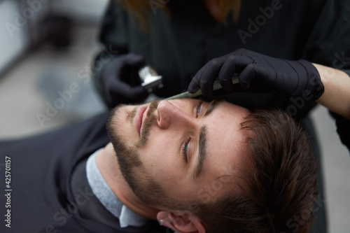 Young beautiful caucasian woman hairdresser cuts beard handsome man at modern barbershop
