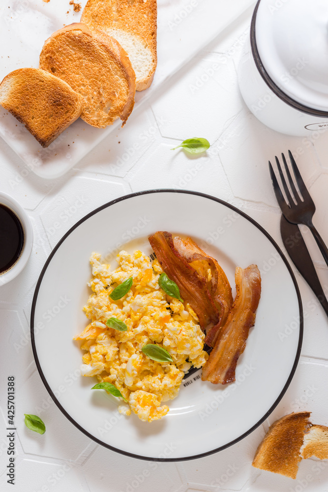 Breakfast for one person with scrambled eggs, bacon and coffee and toast, top view, selective focus