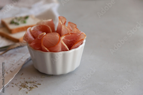 Jerky meat in white bowl on light gray background with fork, knife and bread. There is a copy space. This kind of jerky or dried meat is also known in some traditional kitchens as 