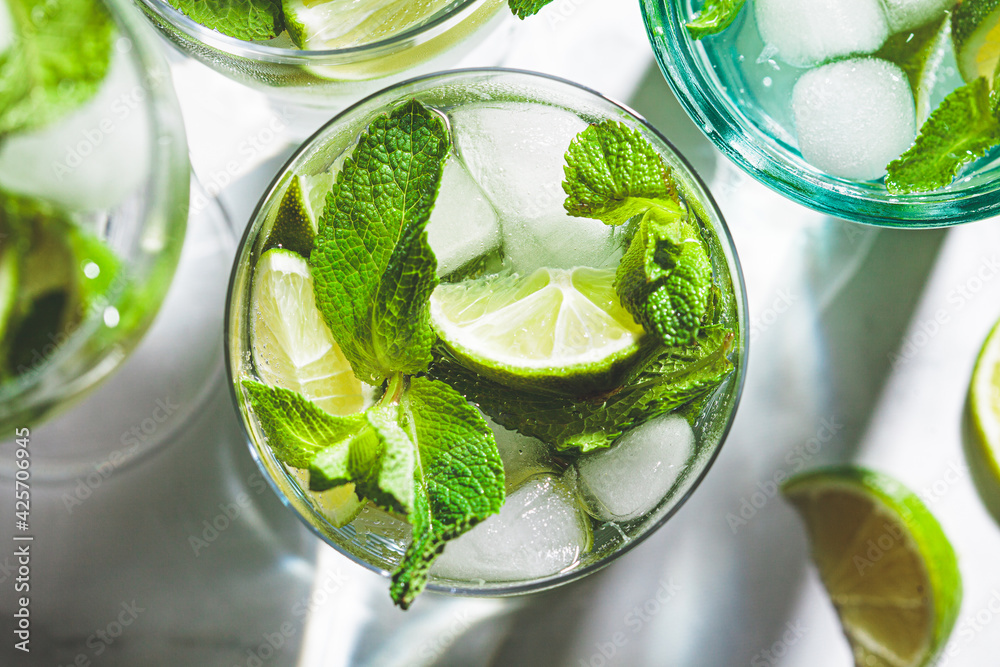 Mojito cocktail with mint and lime in glasses, white marble background, top view, close up.. Refreshing drink with lime and mint in glasses. Mojito cocktail with mint and lime in glasses, white marble background, top view, close up.. Refreshing drink with lime and mint in glasses.
