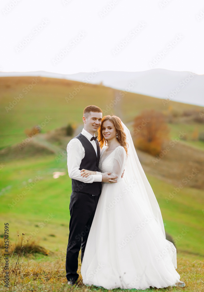 Amazing couple wedding newlyweds in a white dress and a suit walking on the mountain backround, sunset.