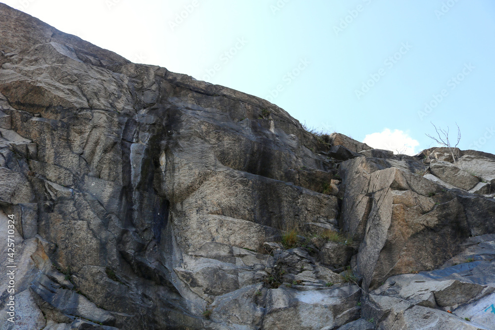gray rocky mountain with black grooves furrowing its reliefs and a blue sky in the background