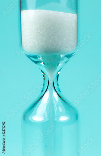 Sand clock on turquoise background. Hourglass as time passing concept. Close up photo.