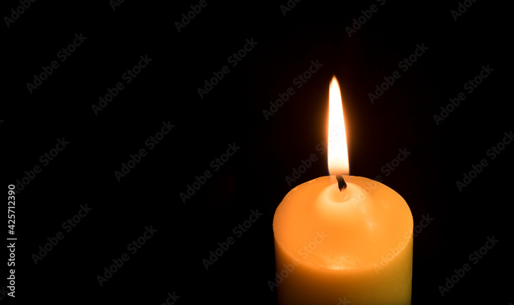 One candle is lit in the dark or on a black background.