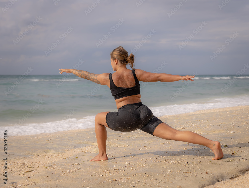Young woman practicing yoga. Standing in Virabhadrasana II pose, Warrior II Pose. Work out. Healthy lifestyle. Strong body. Ocean background. Yoga retreat. Thomas beach, Bali Young woman practicing yoga. Standing in Virabhadrasana II pose, Warrior II Pose. Work out. Healthy lifestyle. Strong body. Ocean background. Yoga retreat. Thomas beach, Bali