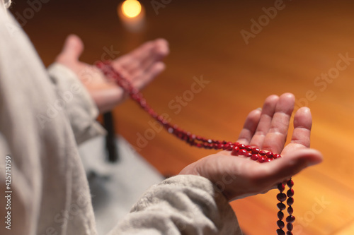 Male hands hold red rosary for prayer and practice in a dark room by candlelight